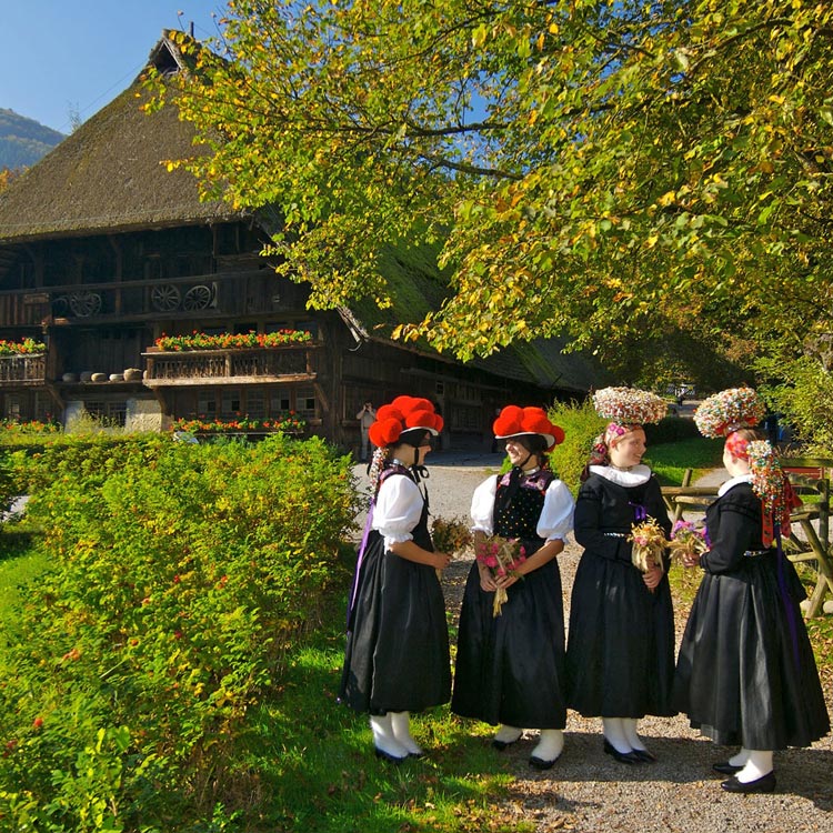 Damen in traditioneller Tracht die vor einem Gebäude bei den Vogtsbauernhöfen